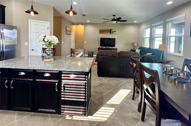 kitchen featuring ceiling fan, a center island, light stone counters, and decorative light fixtures