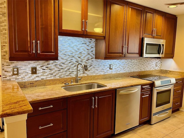 kitchen featuring appliances with stainless steel finishes, backsplash, light stone counters, sink, and light tile patterned floors