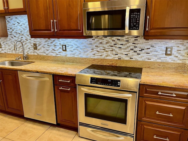 kitchen featuring tasteful backsplash, light stone counters, stainless steel appliances, sink, and light tile patterned floors