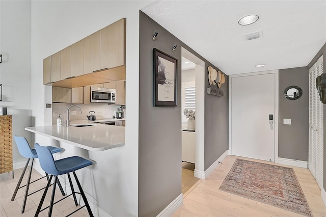 kitchen with kitchen peninsula, light hardwood / wood-style flooring, a breakfast bar area, and sink