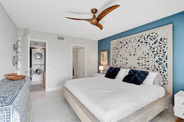 bedroom with ceiling fan, light wood-type flooring, and stacked washer and dryer