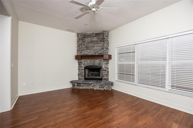 unfurnished living room featuring hardwood / wood-style floors, a textured ceiling, a stone fireplace, and ceiling fan