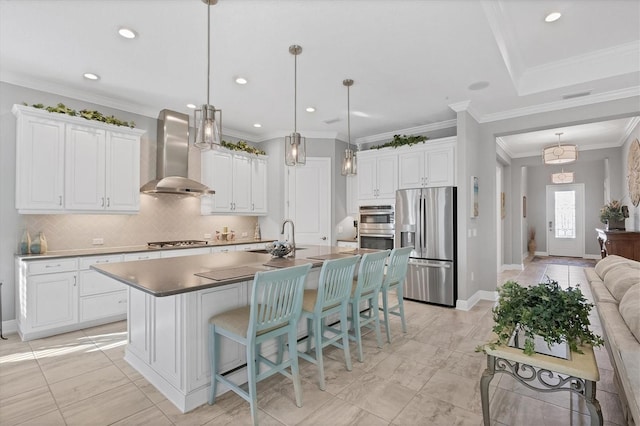 kitchen featuring a center island with sink, wall chimney exhaust hood, white cabinetry, and stainless steel appliances