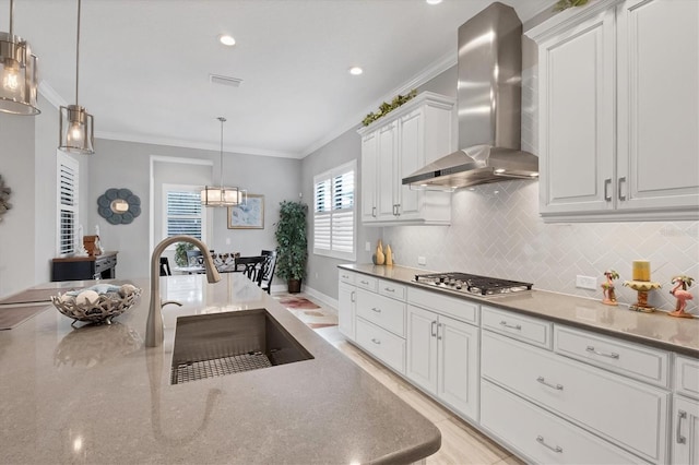 kitchen with white cabinetry, sink, wall chimney exhaust hood, hanging light fixtures, and stainless steel gas cooktop