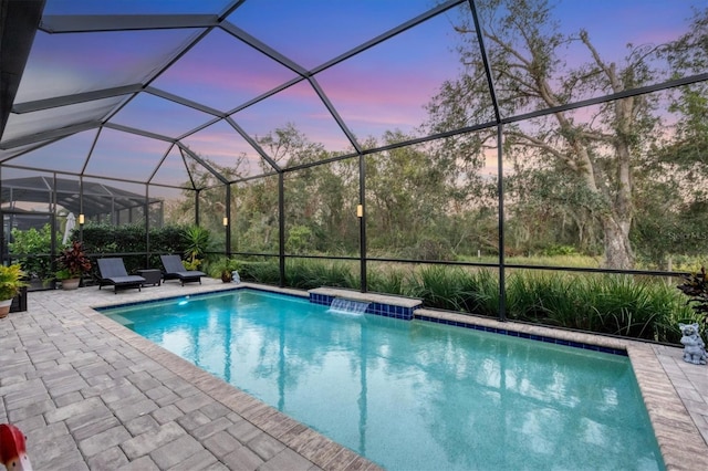 pool at dusk featuring pool water feature, a patio area, and a lanai