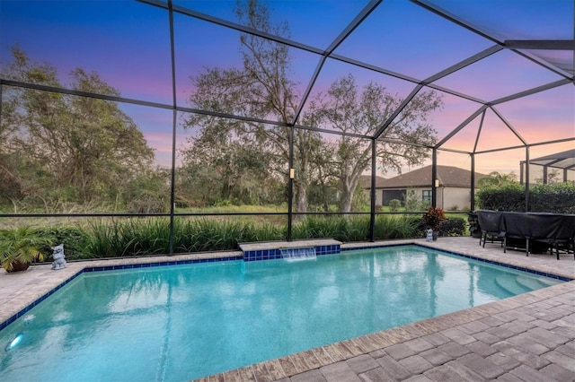 pool at dusk with pool water feature, glass enclosure, and a patio area