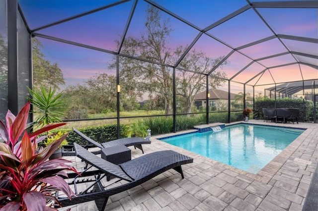 pool at dusk featuring glass enclosure and a patio area