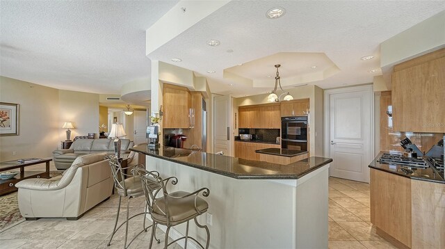 kitchen with kitchen peninsula, tasteful backsplash, a breakfast bar, a tray ceiling, and black double oven