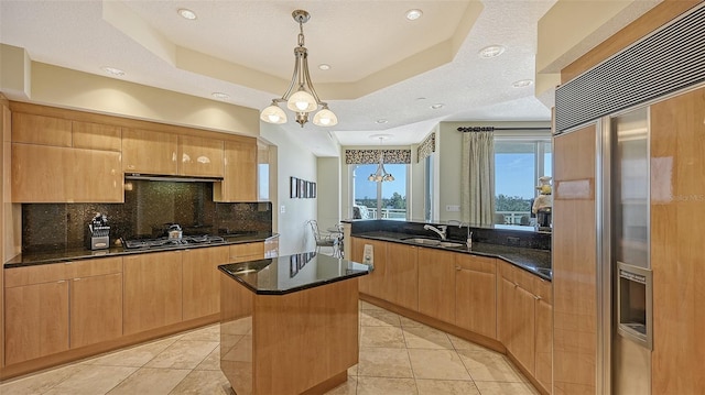 kitchen featuring a tray ceiling, tasteful backsplash, paneled fridge, a kitchen island, and stainless steel gas cooktop