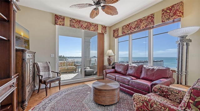 living room with wood-type flooring, a water view, ceiling fan, and a healthy amount of sunlight