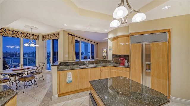 kitchen with pendant lighting, paneled built in fridge, sink, dark stone countertops, and light brown cabinetry