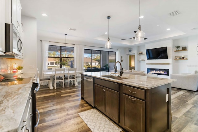 kitchen with white cabinetry, light stone countertops, stainless steel appliances, a tray ceiling, and a fireplace