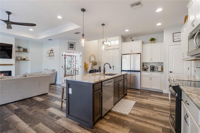 kitchen with dark wood-type flooring, tasteful backsplash, a center island with sink, white cabinets, and appliances with stainless steel finishes