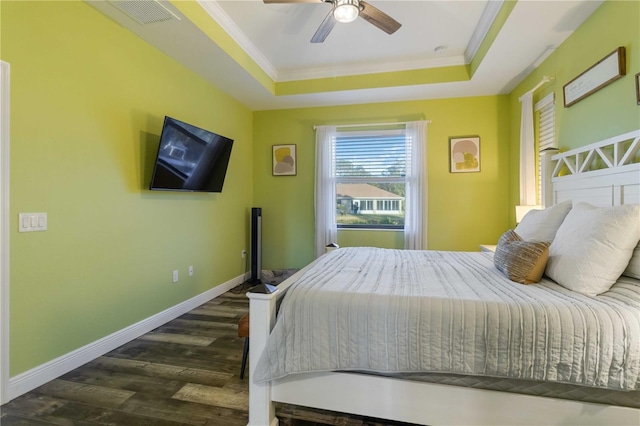 bedroom with dark hardwood / wood-style floors, ceiling fan, ornamental molding, and a tray ceiling