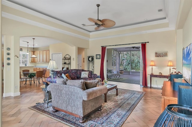 living room featuring light parquet flooring, a tray ceiling, ceiling fan, and ornamental molding