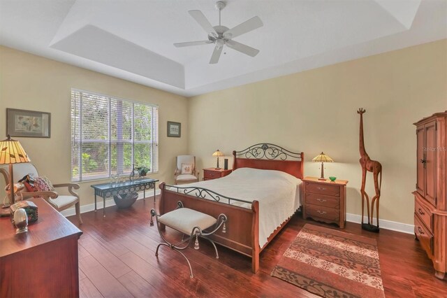 bedroom with dark hardwood / wood-style flooring, a raised ceiling, and ceiling fan