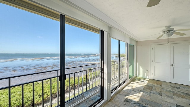 unfurnished sunroom featuring a view of the beach, a water view, and ceiling fan