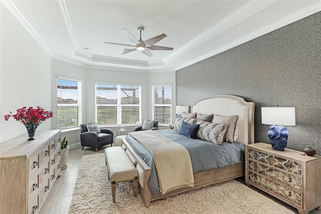 bedroom with light wood-type flooring, a tray ceiling, ceiling fan, and ornamental molding