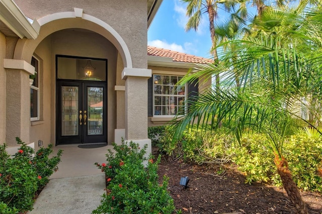 view of exterior entry featuring french doors, a tile roof, and stucco siding