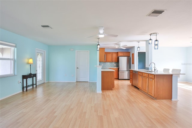 kitchen featuring light wood-type flooring, tasteful backsplash, stainless steel appliances, a kitchen island, and hanging light fixtures