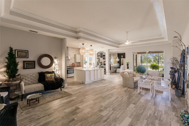 living room with a raised ceiling, ceiling fan, light hardwood / wood-style floors, and ornamental molding