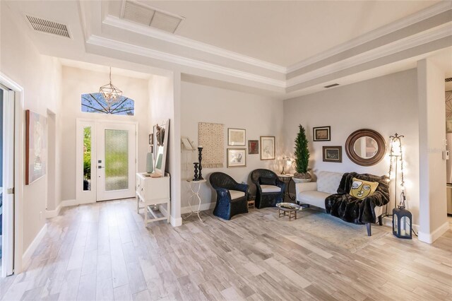 foyer featuring light wood-type flooring, ornamental molding, and a tray ceiling