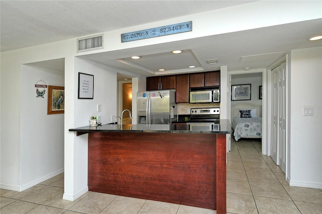 kitchen featuring stainless steel appliances, a raised ceiling, kitchen peninsula, dark brown cabinets, and light tile patterned floors