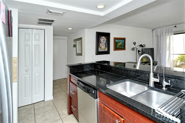 kitchen with light tile patterned floors, stainless steel dishwasher, dark stone counters, and sink