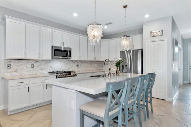 kitchen featuring an island with sink, appliances with stainless steel finishes, decorative light fixtures, white cabinets, and sink