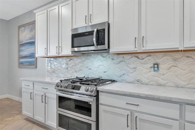 kitchen with light stone countertops, appliances with stainless steel finishes, white cabinetry, tasteful backsplash, and light tile patterned flooring