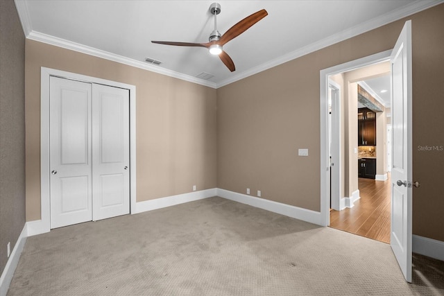 unfurnished bedroom with crown molding, ceiling fan, a closet, and light colored carpet