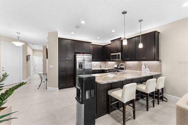 kitchen featuring dark brown cabinetry, appliances with stainless steel finishes, decorative light fixtures, and kitchen peninsula