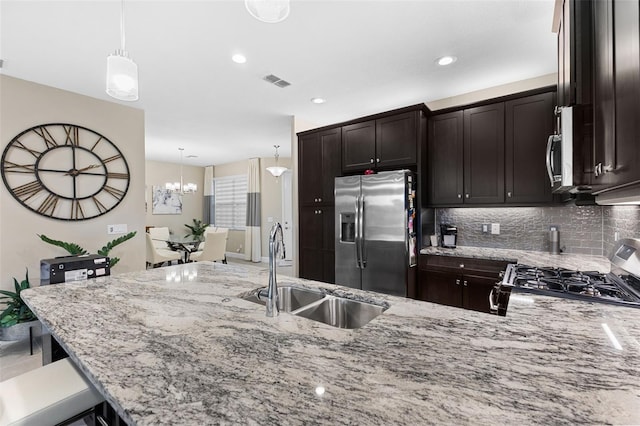 kitchen with sink, appliances with stainless steel finishes, dark brown cabinetry, light stone countertops, and decorative light fixtures