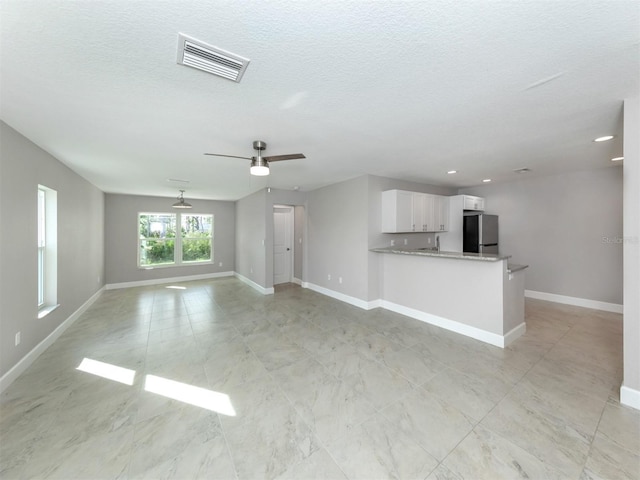 unfurnished living room featuring ceiling fan and a textured ceiling