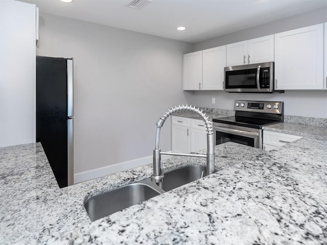 kitchen with white cabinets, appliances with stainless steel finishes, light stone counters, and sink