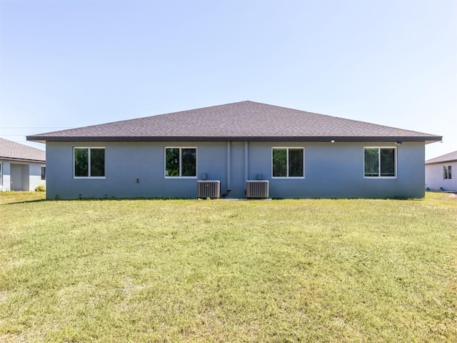 rear view of house with central AC unit and a lawn