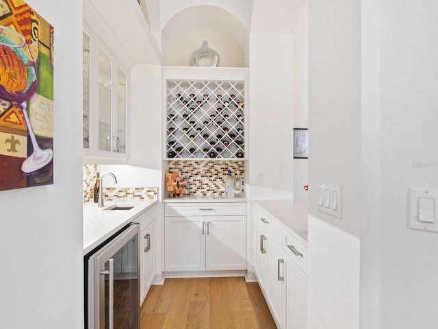 bar with white cabinets, decorative backsplash, sink, and beverage cooler