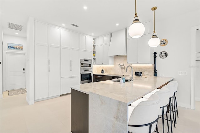 kitchen featuring pendant lighting, white cabinets, light stone countertops, custom range hood, and kitchen peninsula