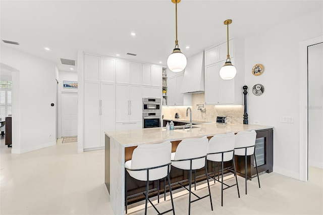 kitchen featuring white cabinetry, a kitchen breakfast bar, kitchen peninsula, pendant lighting, and custom exhaust hood