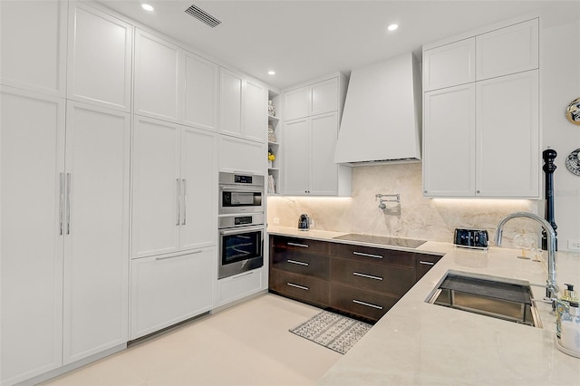 kitchen featuring black electric stovetop, tasteful backsplash, custom exhaust hood, sink, and white cabinetry