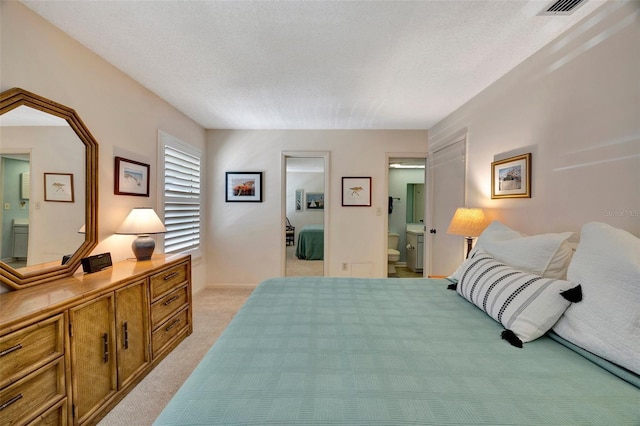 bedroom with a textured ceiling, ensuite bathroom, and light carpet