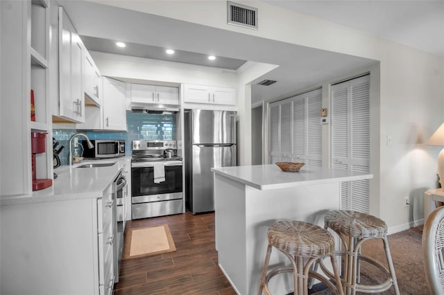 kitchen featuring white cabinets, a kitchen breakfast bar, sink, tasteful backsplash, and stainless steel appliances