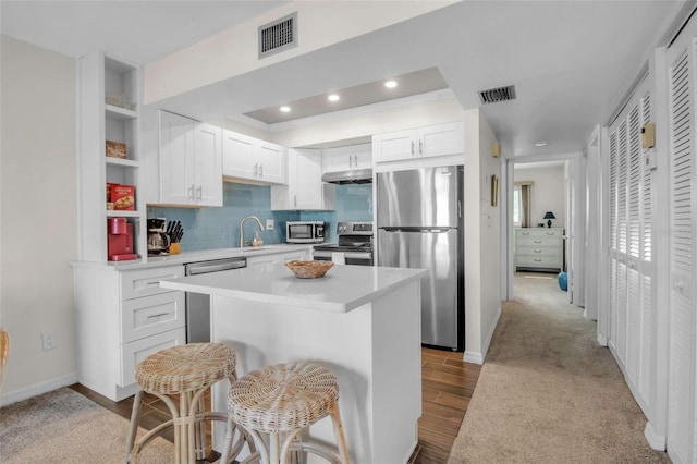 kitchen featuring a kitchen bar, appliances with stainless steel finishes, tasteful backsplash, white cabinets, and a center island