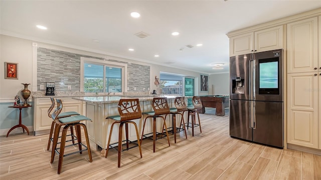 kitchen featuring stainless steel fridge, light stone counters, a breakfast bar area, and billiards