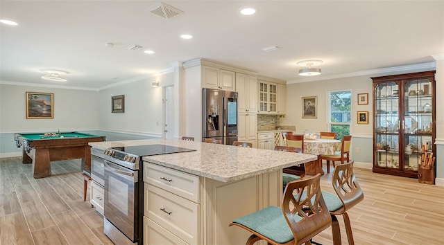 kitchen with light wood-type flooring, ornamental molding, stainless steel appliances, cream cabinets, and pool table