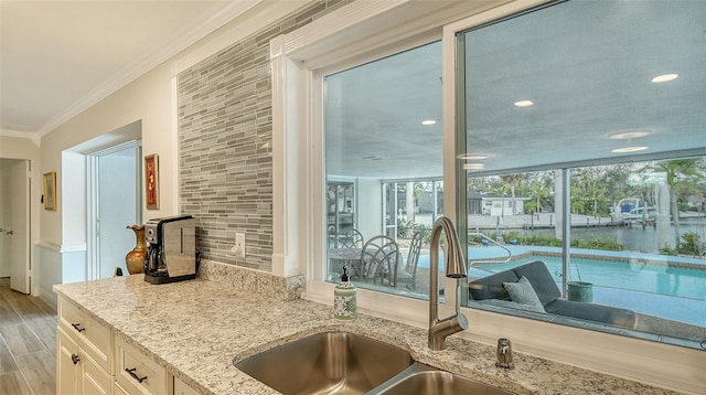 kitchen with white cabinetry, sink, light stone counters, light wood-type flooring, and ornamental molding