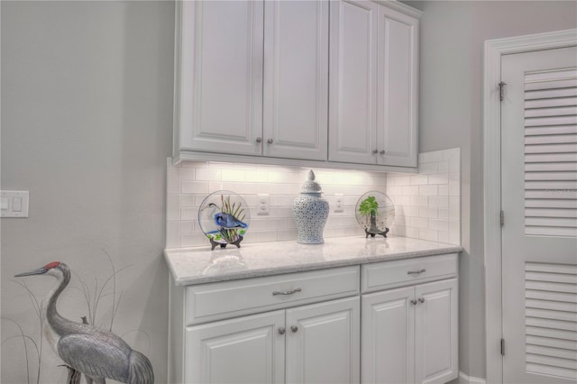 interior space with light stone countertops, white cabinetry, and backsplash