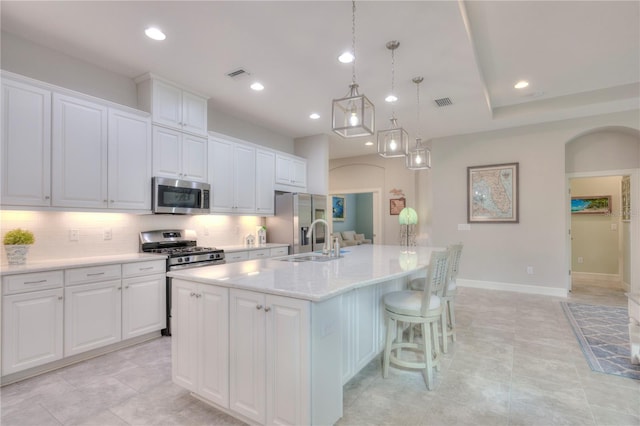 kitchen with white cabinetry, an island with sink, stainless steel appliances, and decorative light fixtures