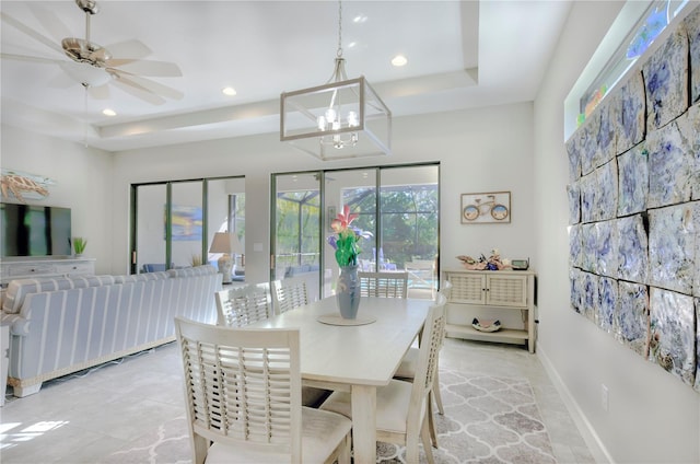 tiled dining area with a tray ceiling and ceiling fan with notable chandelier