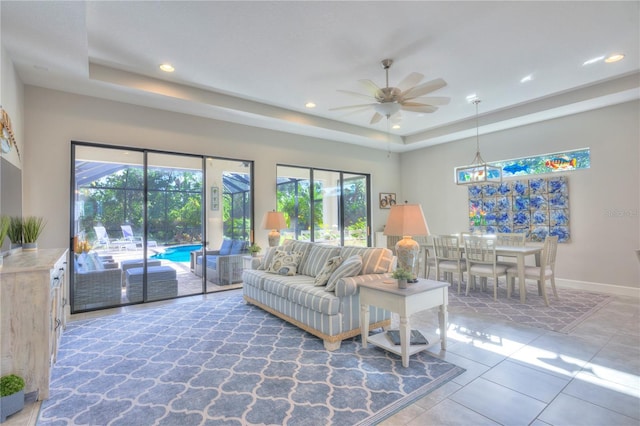 living room with tile patterned flooring, ceiling fan, a wealth of natural light, and a tray ceiling